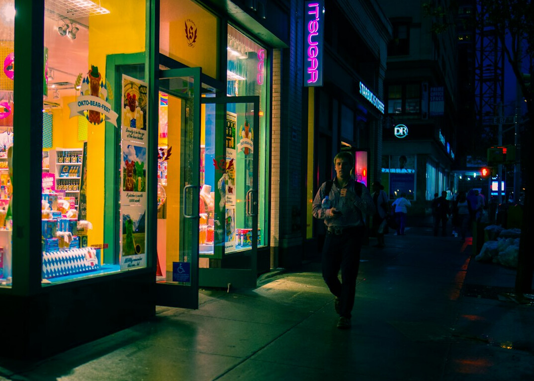 Pedestrians walking past illuminated shopfronts at night